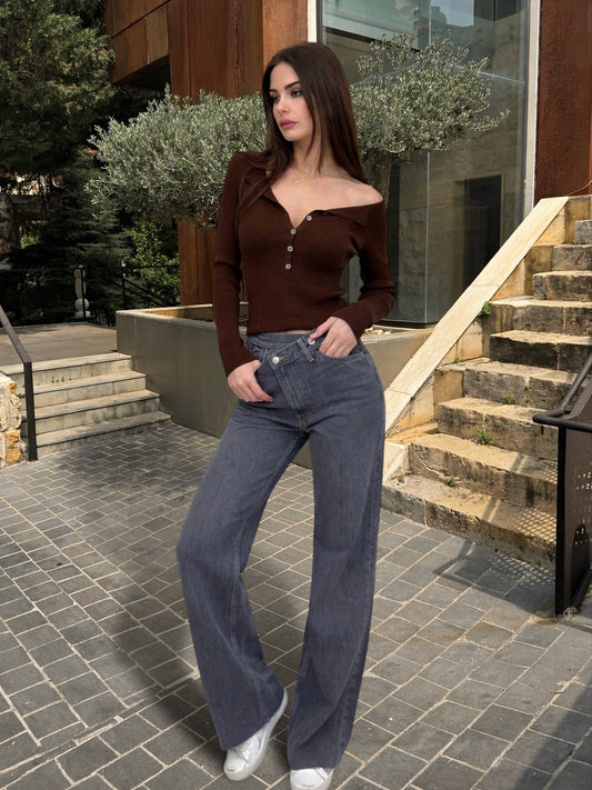 Woman in brown top and blue jeans standing on a stone pavement with steps and plants in the background