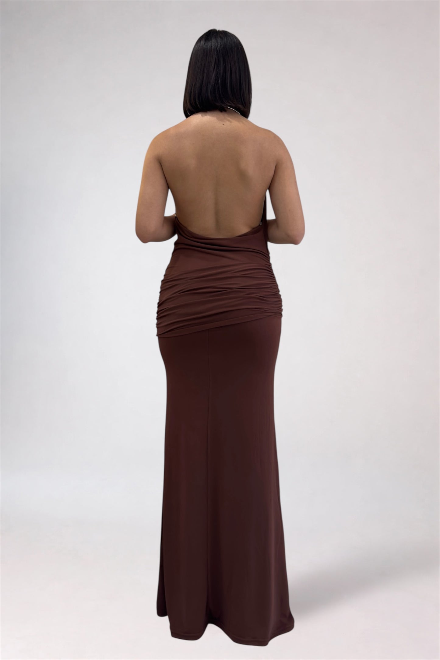 Woman wearing a brown halter neck gown on a plain background