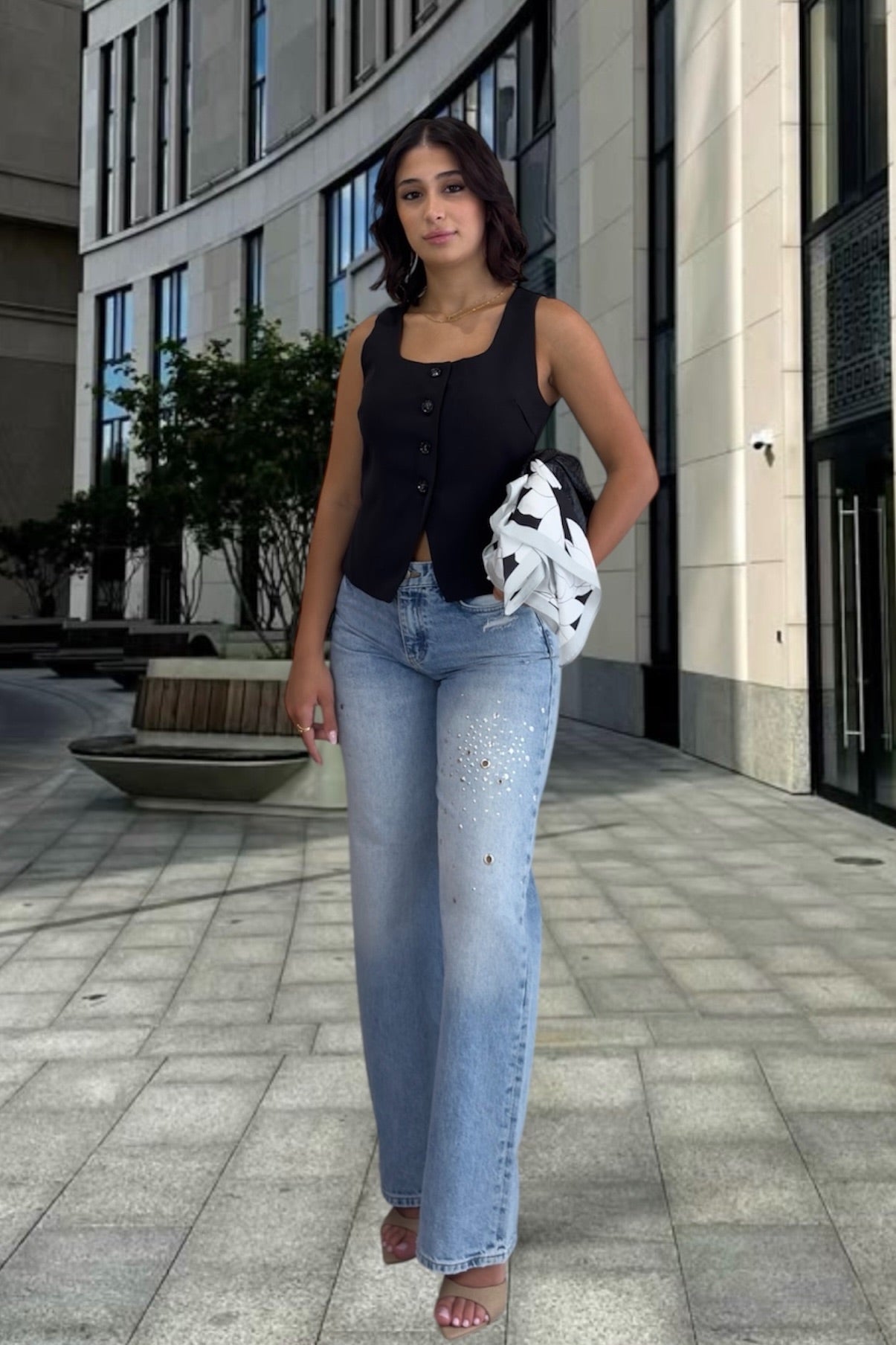 Woman in black sleeveless top and blue jeans standing on a city street.