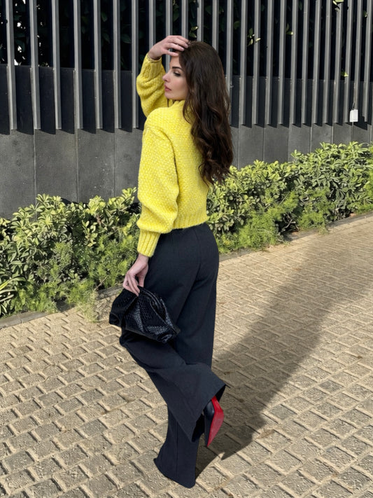 Woman in a yellow sweater and black pants walking outdoors on a paved path.