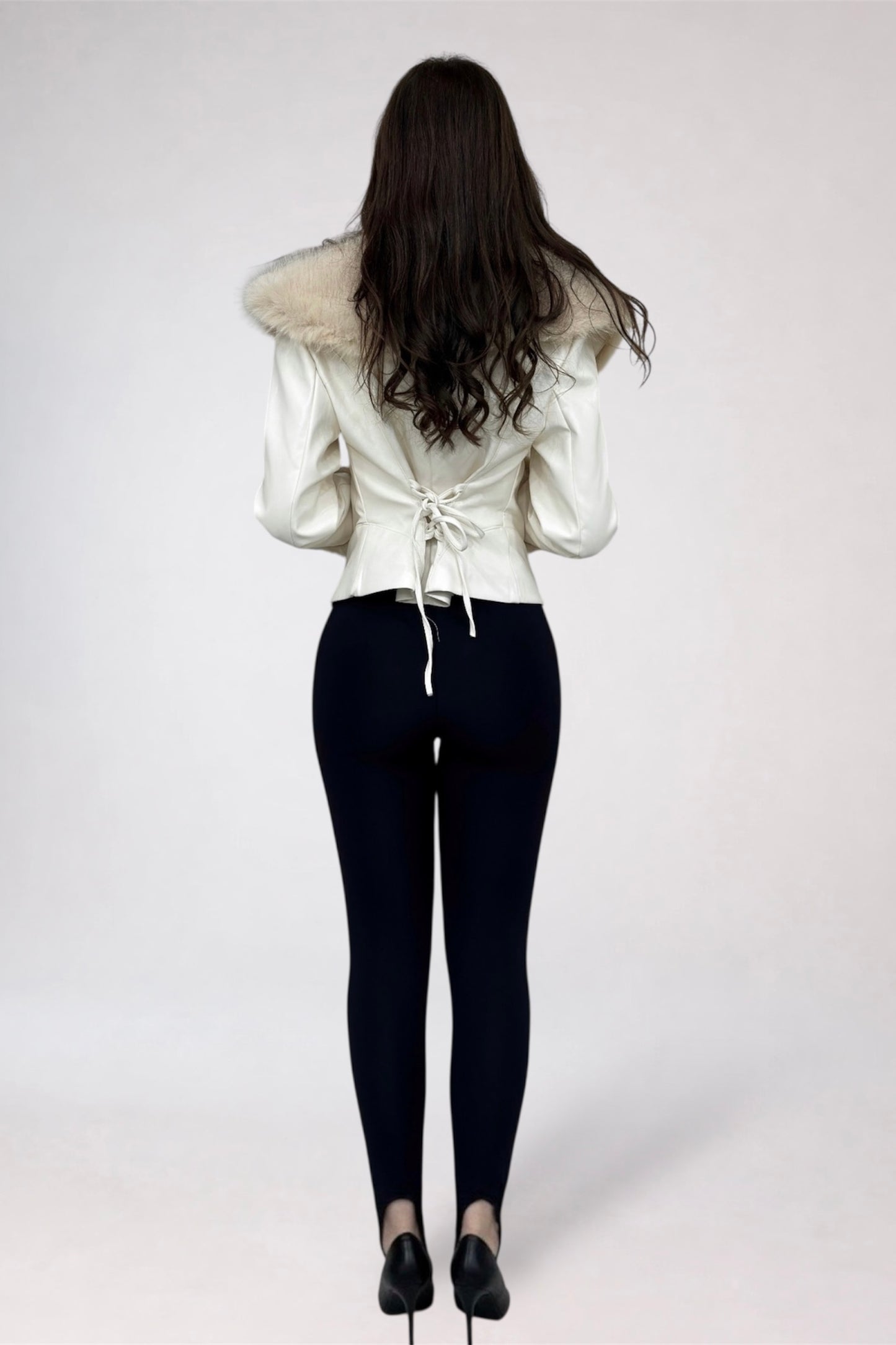 Person wearing a white jacket with fur collar and black pants on a plain background