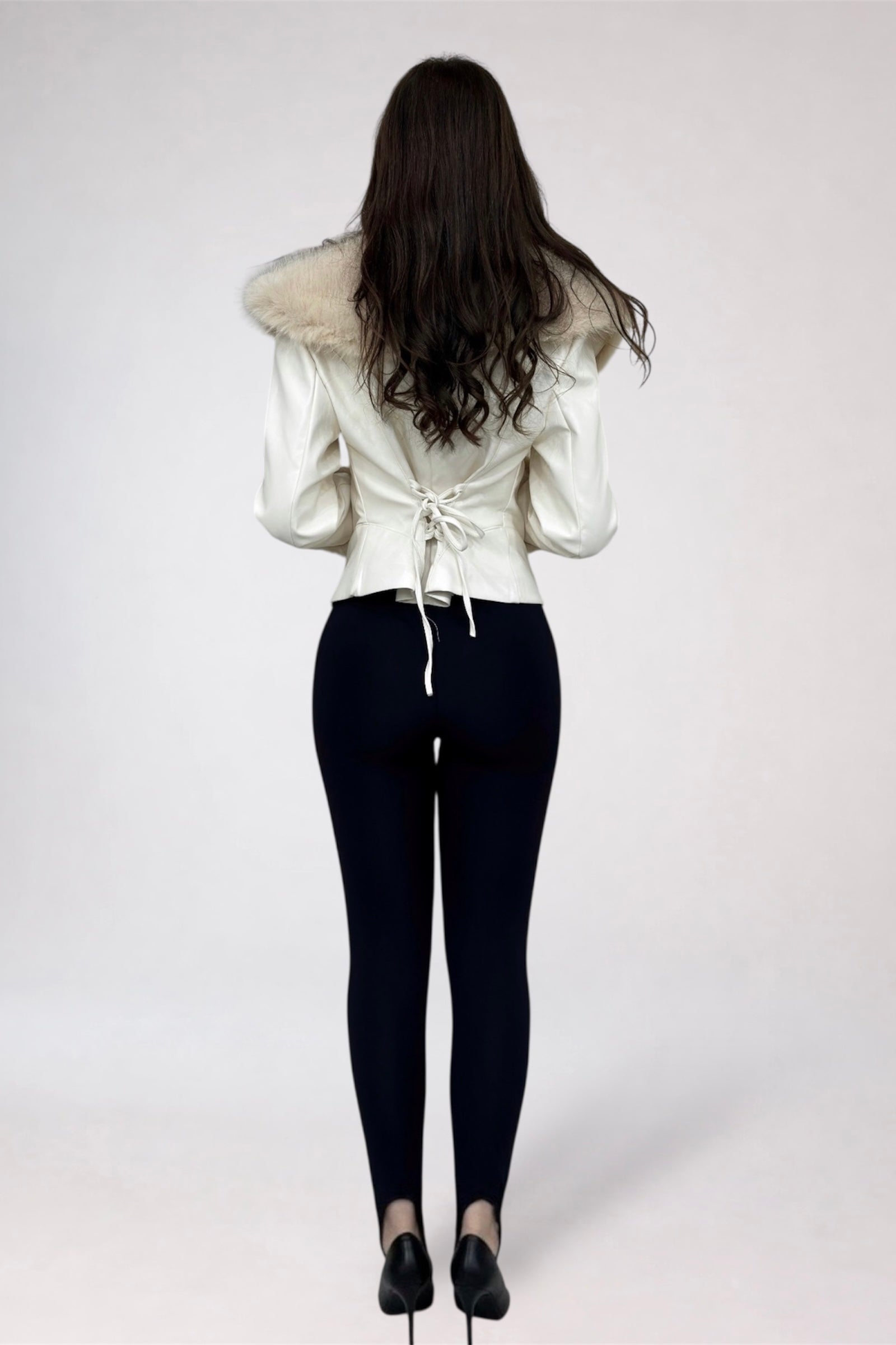 Person wearing a white jacket with fur collar and black pants on a plain background