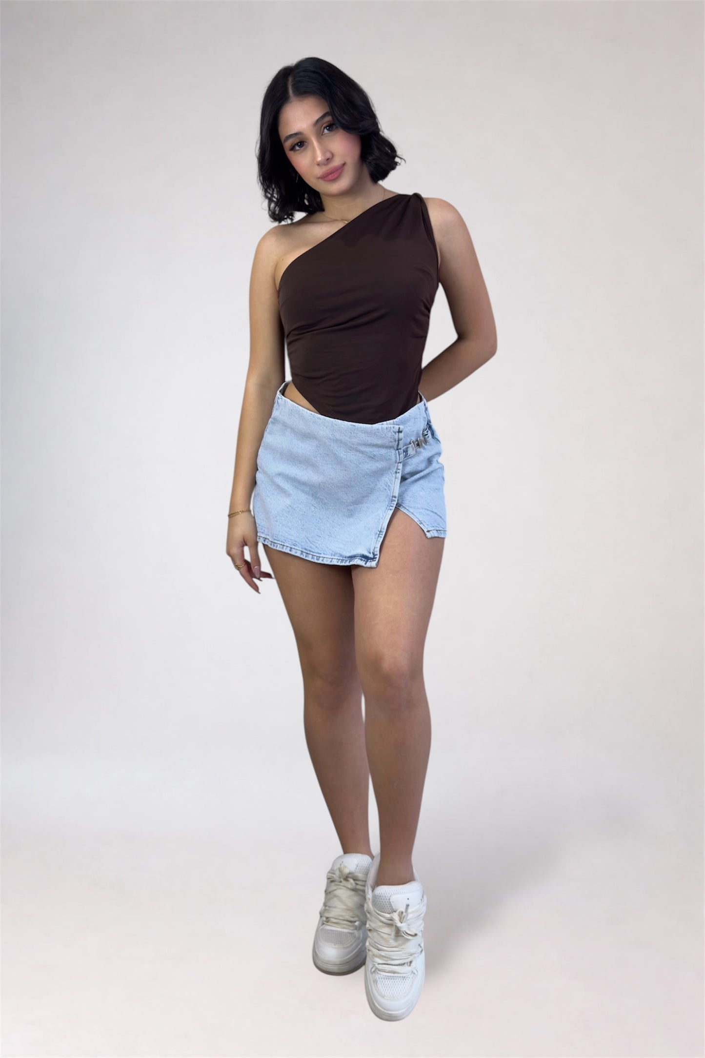 Woman wearing a brown one-shoulder top and light blue denim shorts on a white background