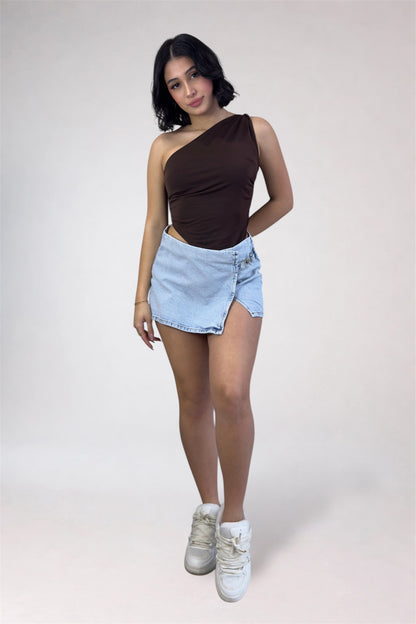 Woman wearing a brown one-shoulder top and light blue denim shorts on a white background