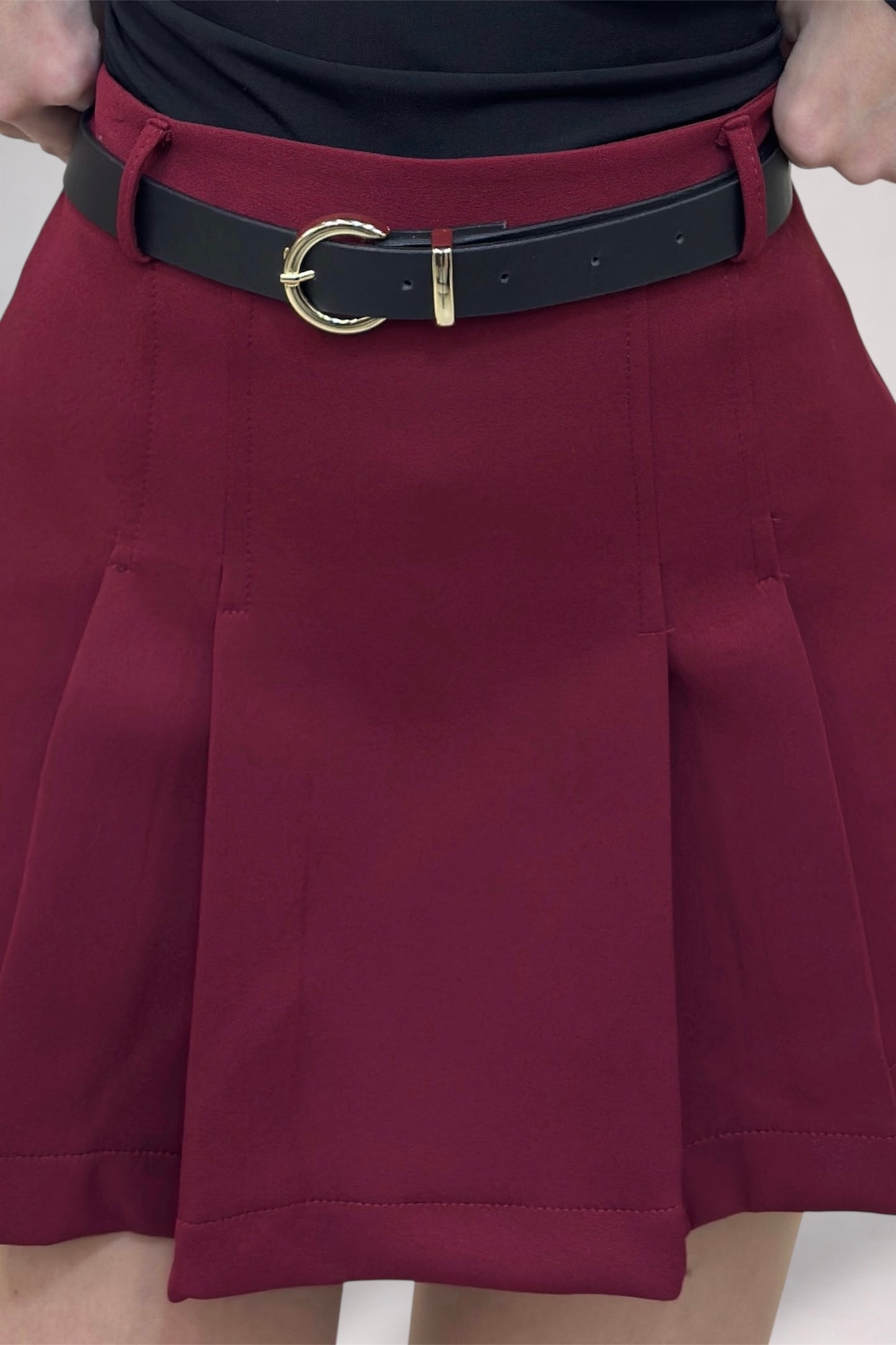 Maroon pleated skirt with a black belt and gold buckle on a neutral background