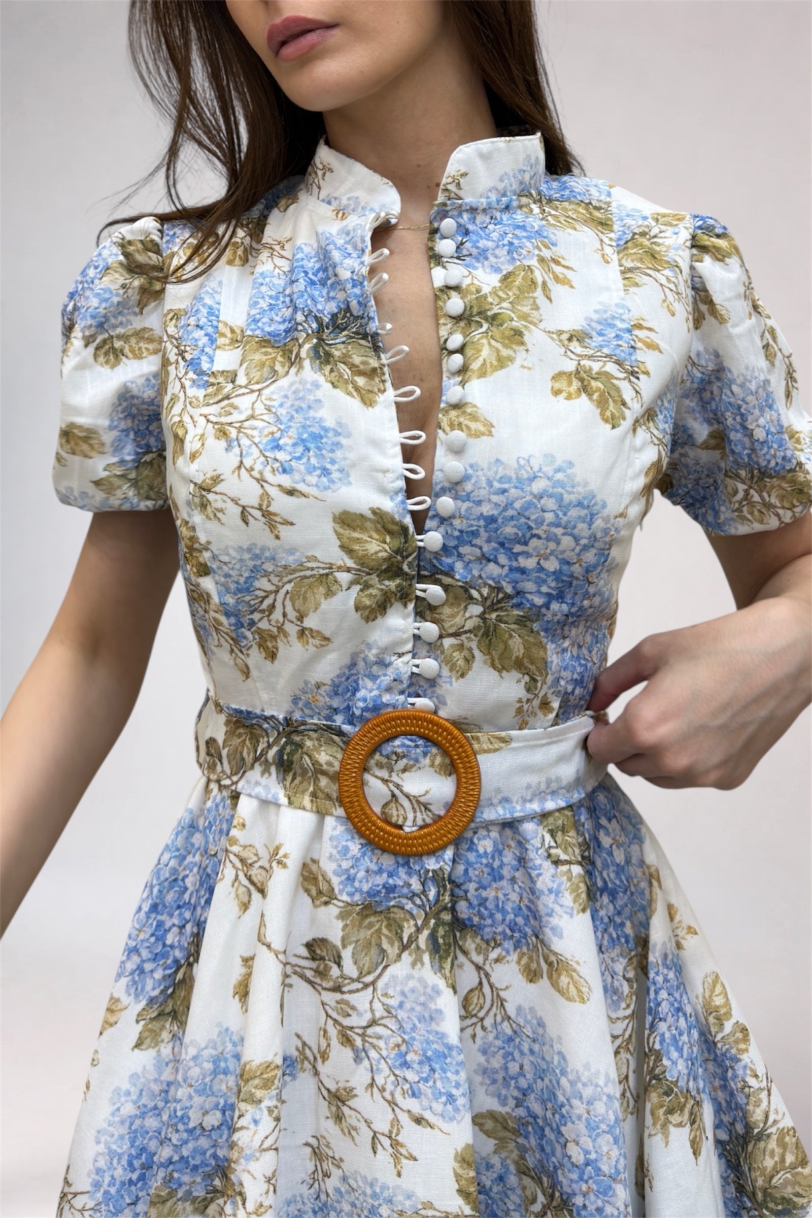 Woman wearing a floral dress with a wooden belt buckle on a plain background