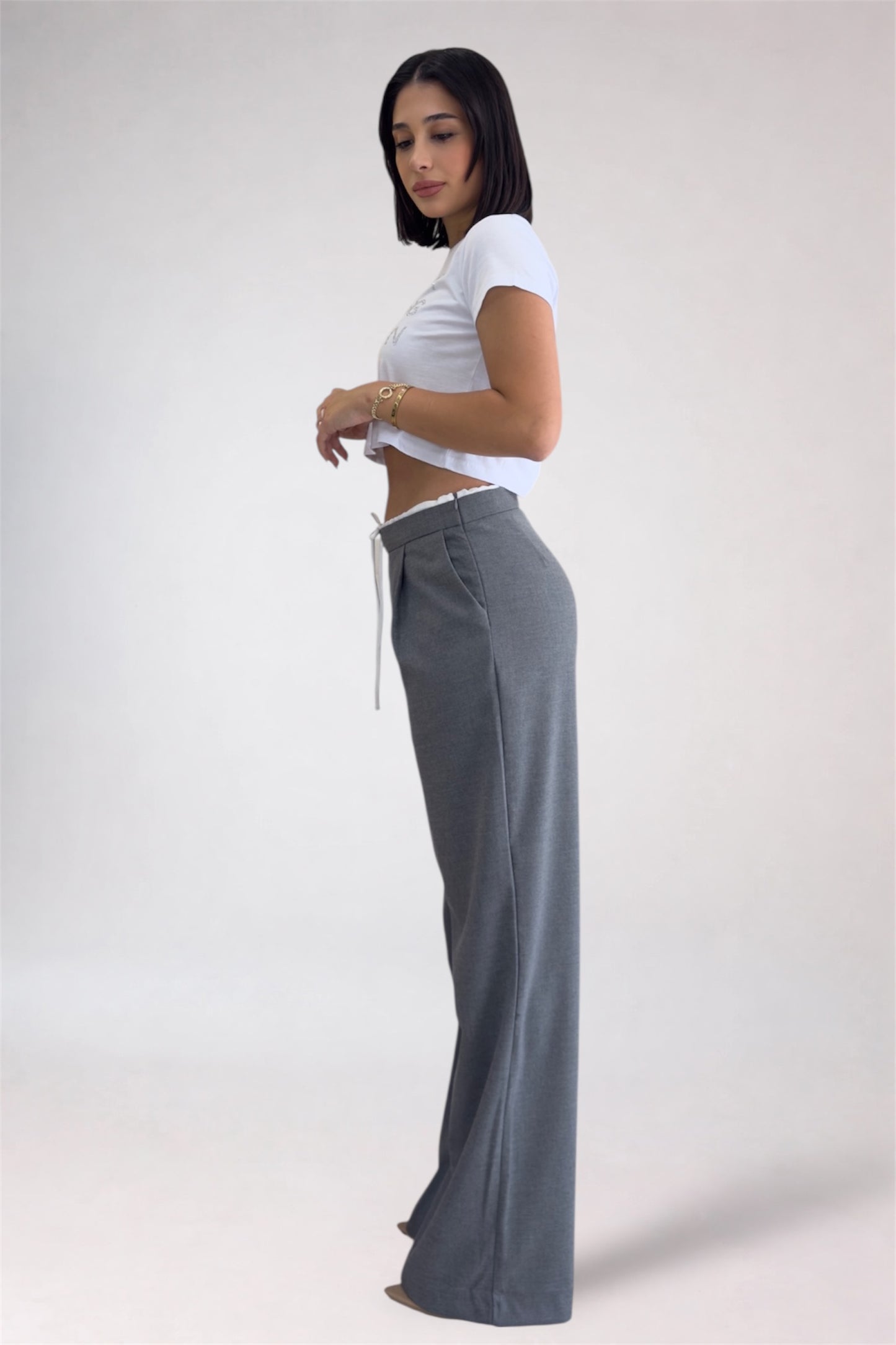 Woman wearing a white crop top and gray wide-leg pants on a plain background