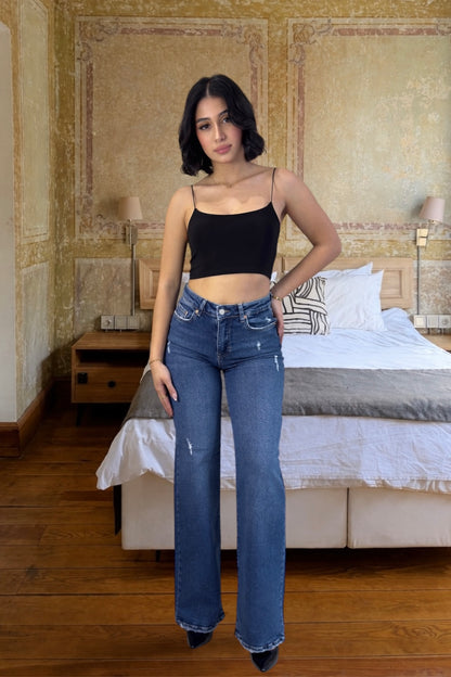 Woman wearing blue jeans and a black top in a bedroom setting