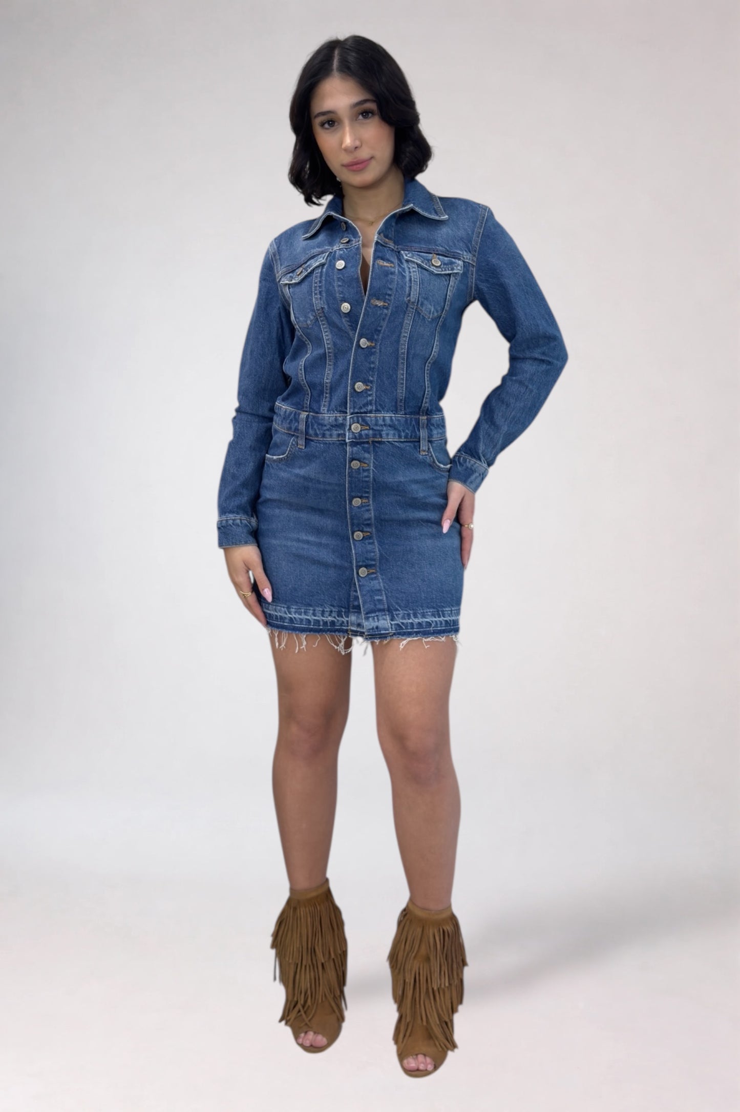 Woman wearing a denim dress with fringed brown boots on a white background