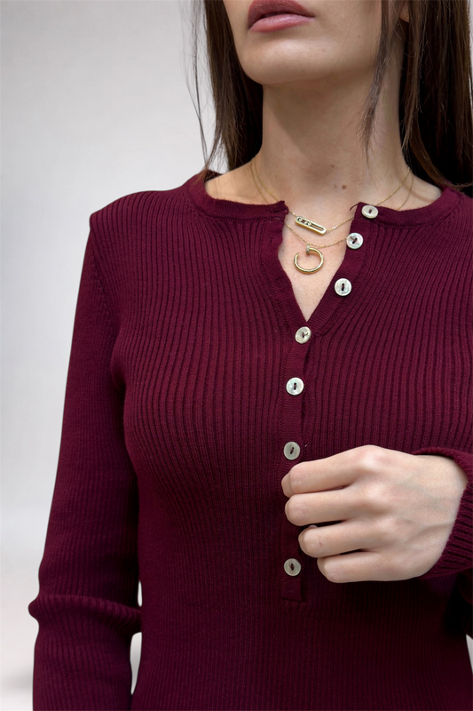 Close-up of a person wearing a burgundy ribbed sweater with buttons on a plain background