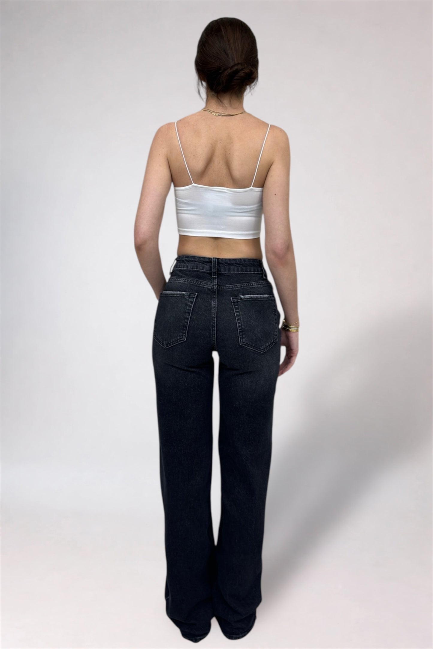 Person wearing a white tank top and dark jeans on a plain background