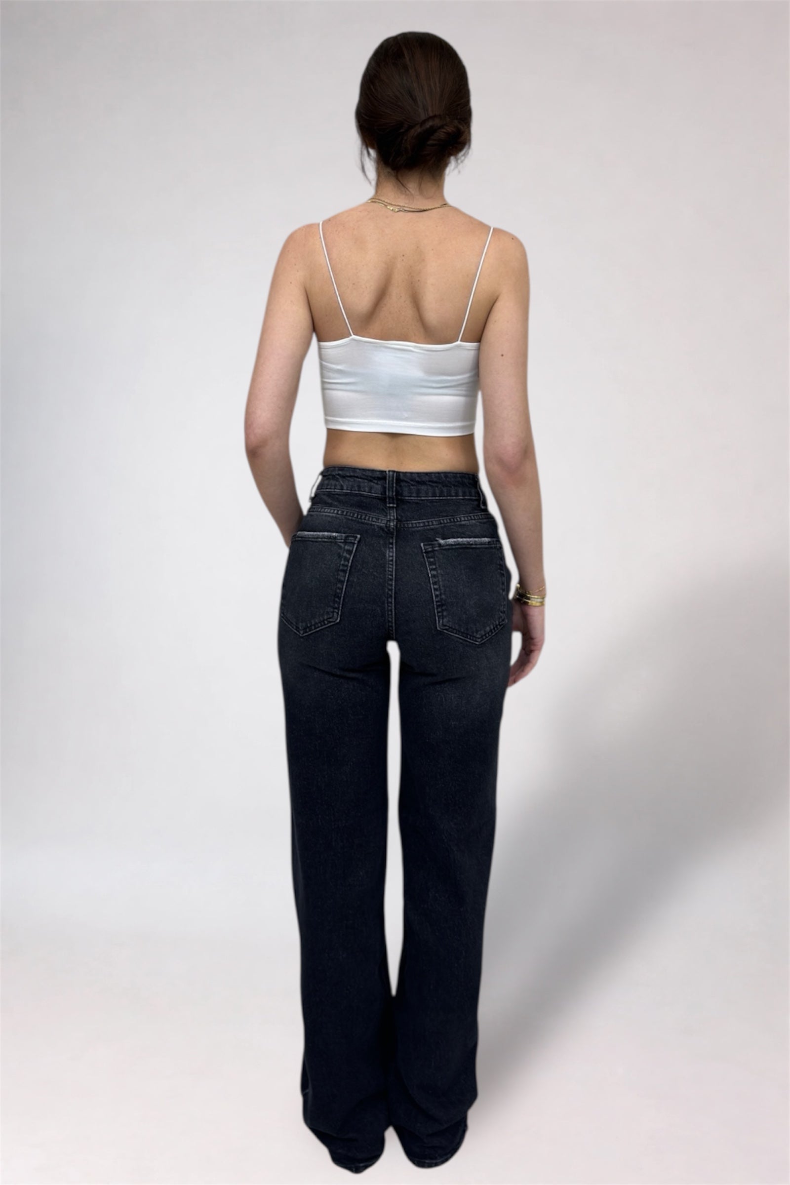 Person wearing a white tank top and dark jeans on a plain background