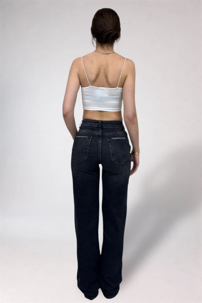 Person wearing a white tank top and dark jeans on a plain background