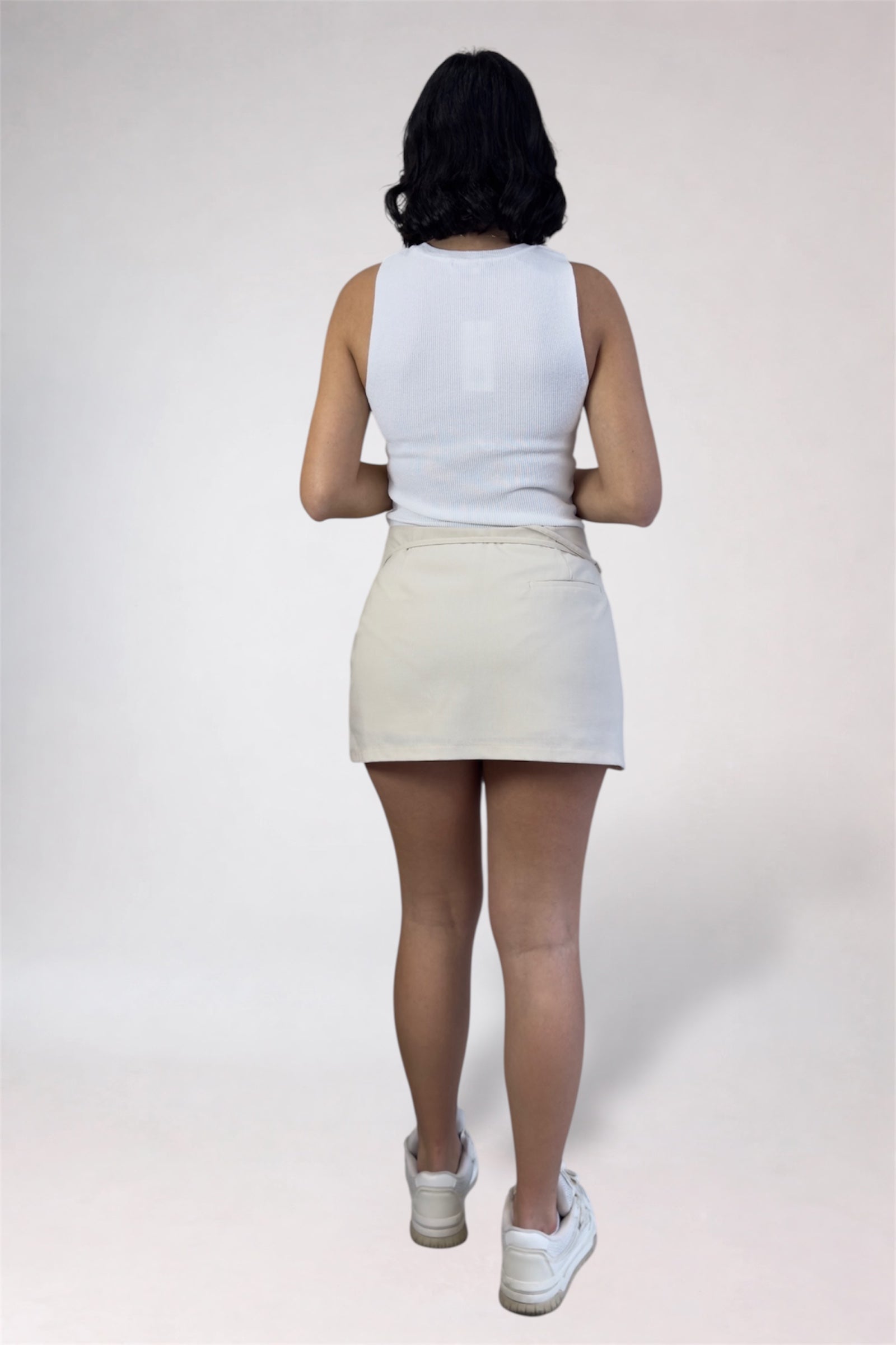 Person wearing a white tank top and cream-colored skirt on a plain background