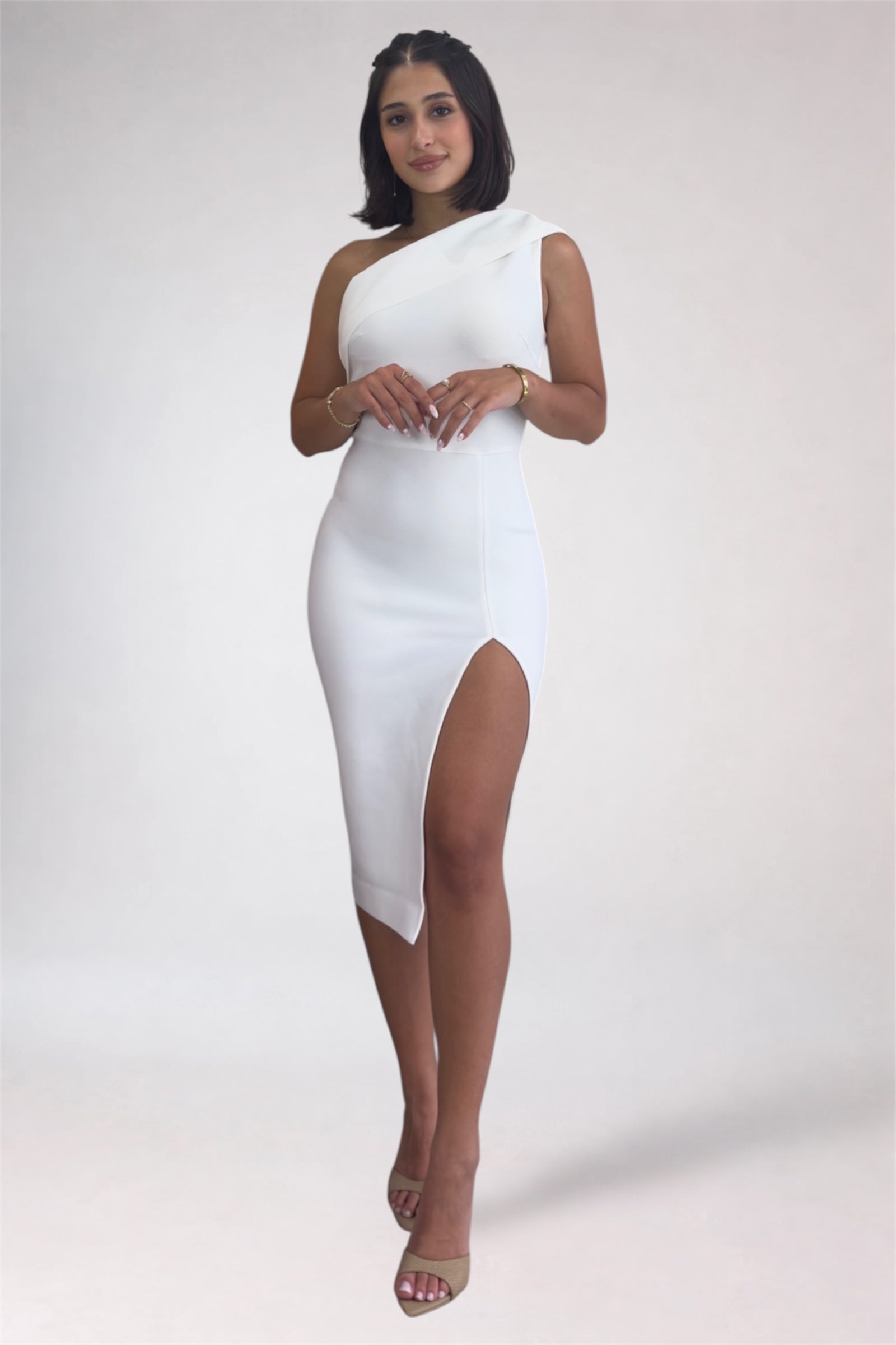 Woman wearing a white one-shoulder dress with a slit on a plain background
