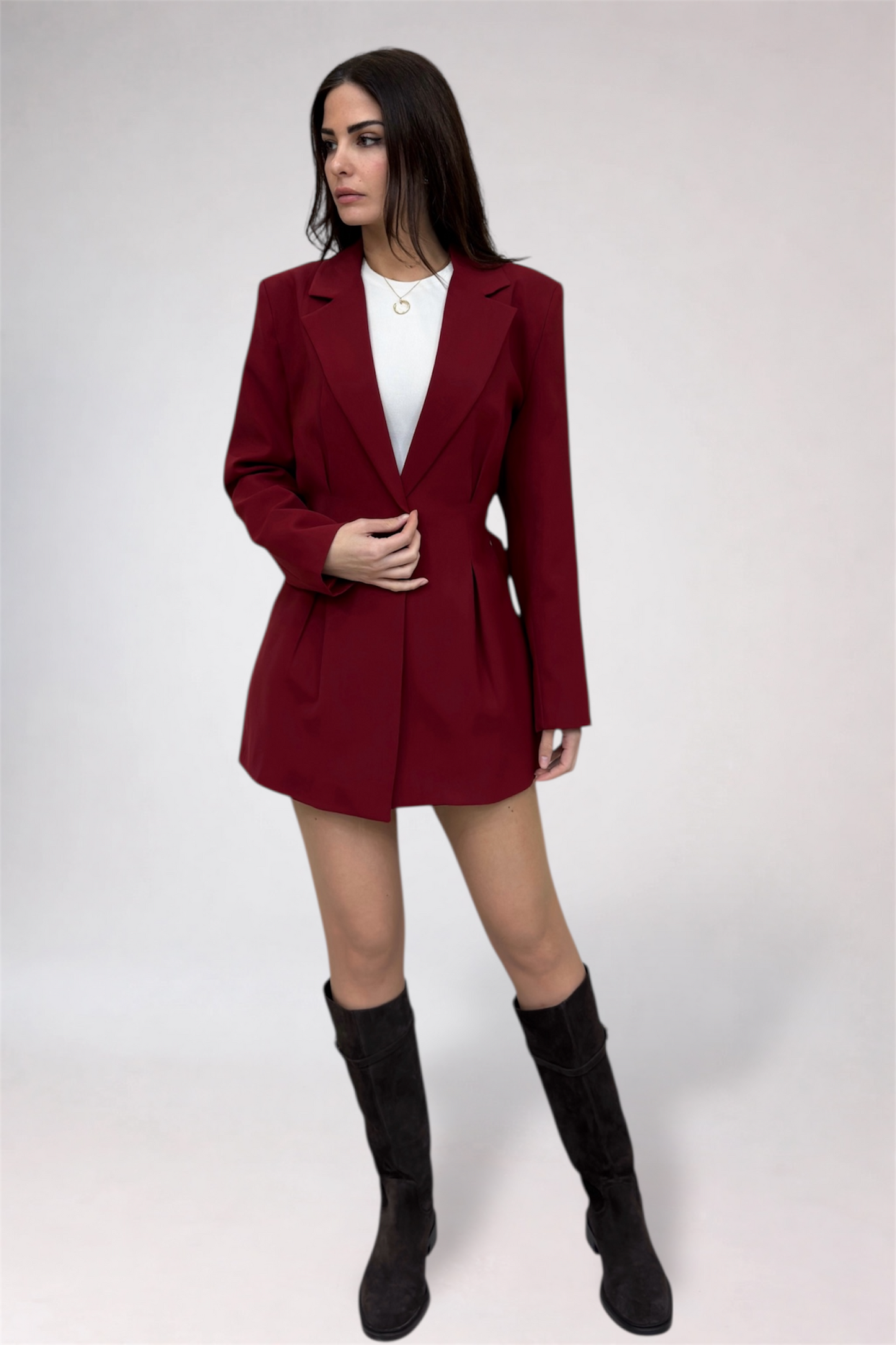 Woman wearing a burgundy blazer dress with black boots on a white background