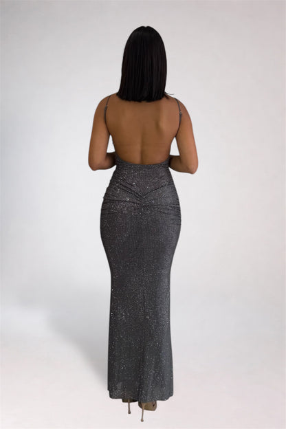 A woman modeling a sparkly, sleeveless, bodycon maxi dress in a shimmering gray color, standing in profile against a light gray studio background.