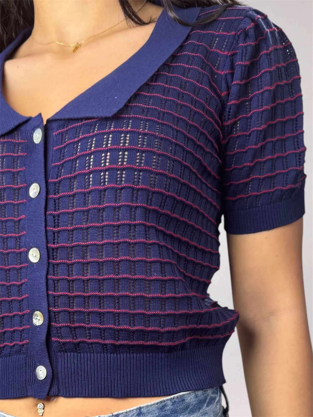 A close-up of a person wearing a short-sleeve knit cardigan top in dark blue with thin pinkish-red horizontal stripes and silver buttons.