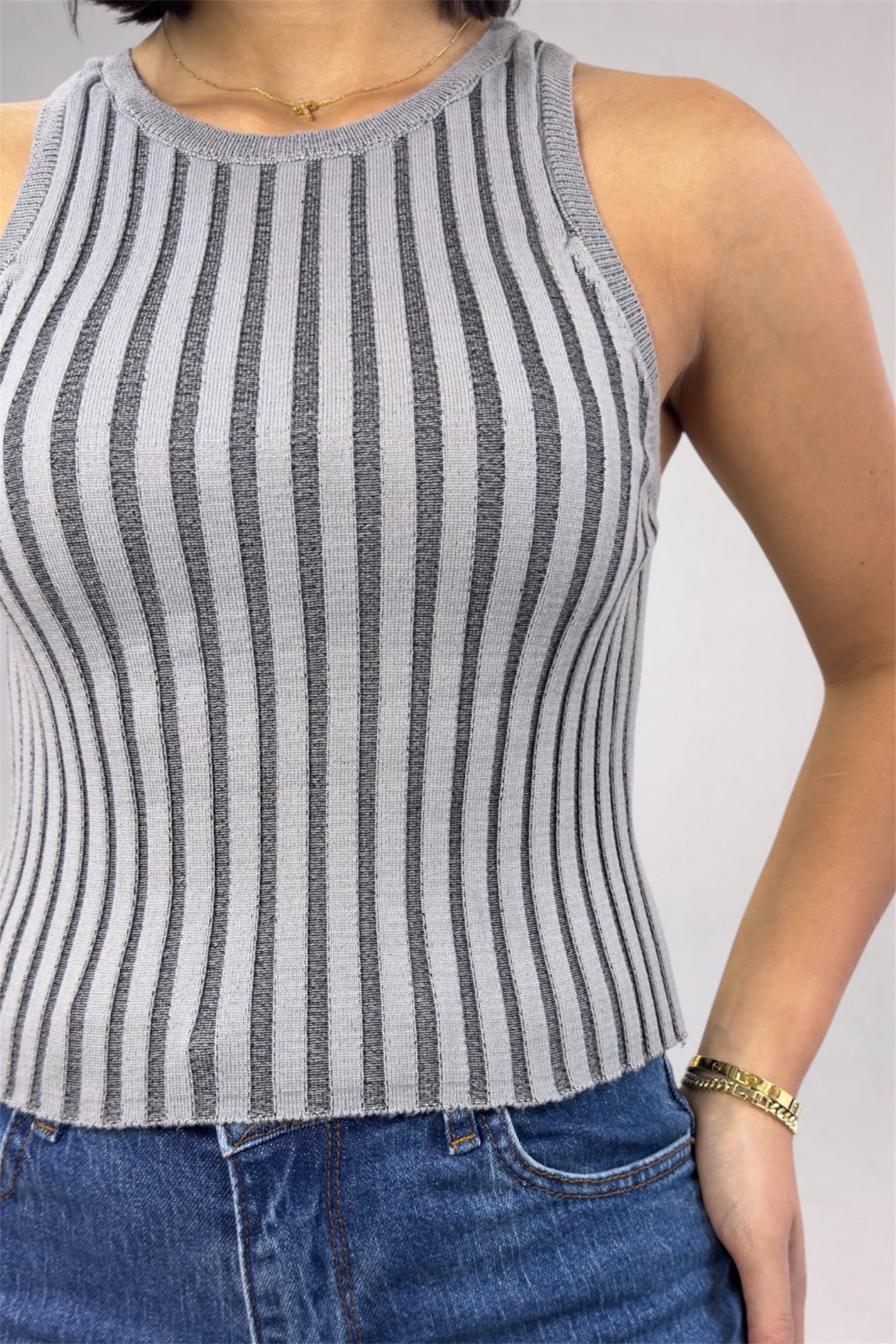 Person wearing a gray and white striped tank top with blue jeans on a plain background