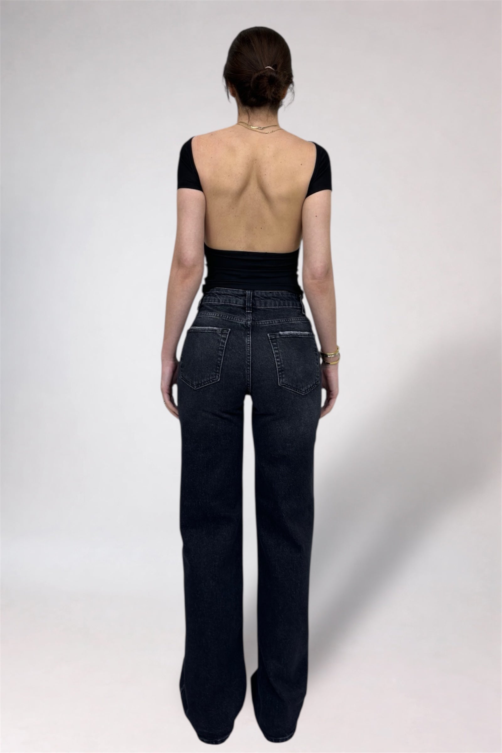 Person wearing black high-waisted jeans and a black crop top on a white background