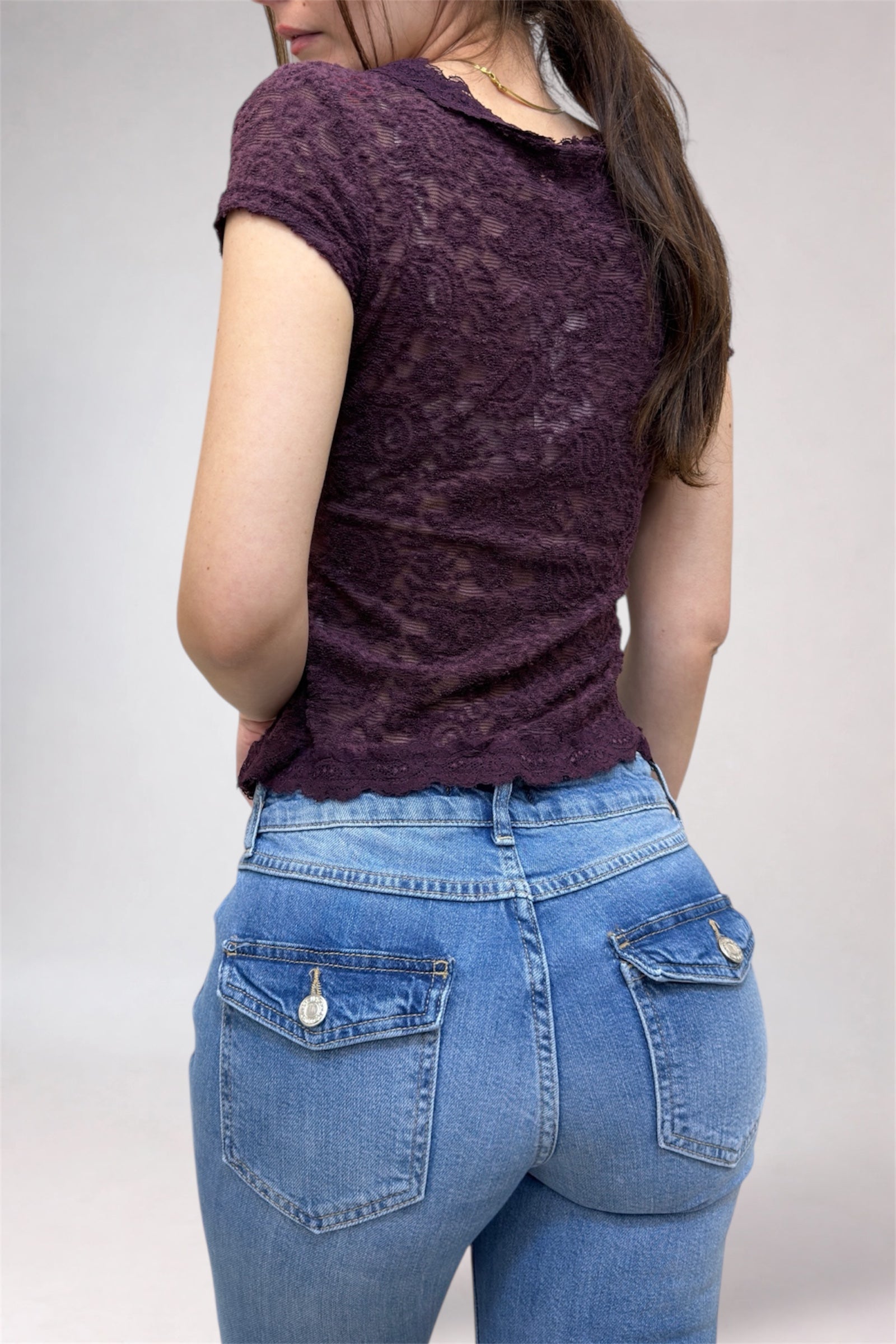 Person wearing a purple lace top and blue jeans on a plain background