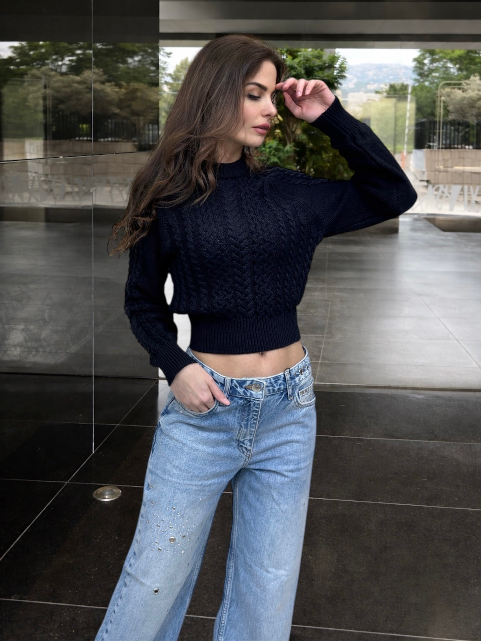 Woman wearing a black sweater and light blue jeans in an outdoor setting.