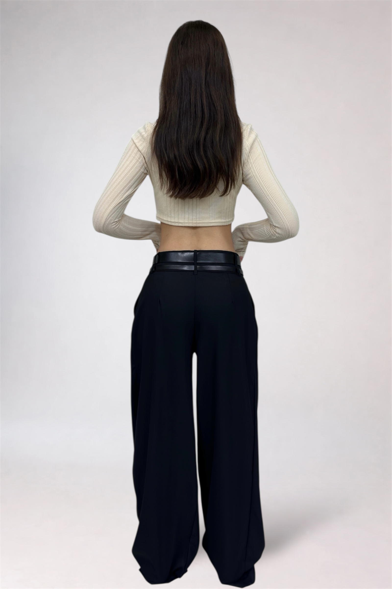 Person wearing a cream long-sleeve top and black wide-leg pants on a white background