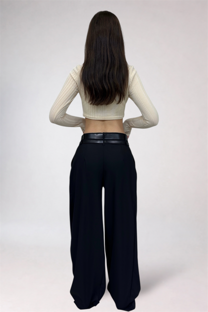 Person wearing a cream long-sleeve top and black wide-leg pants on a white background