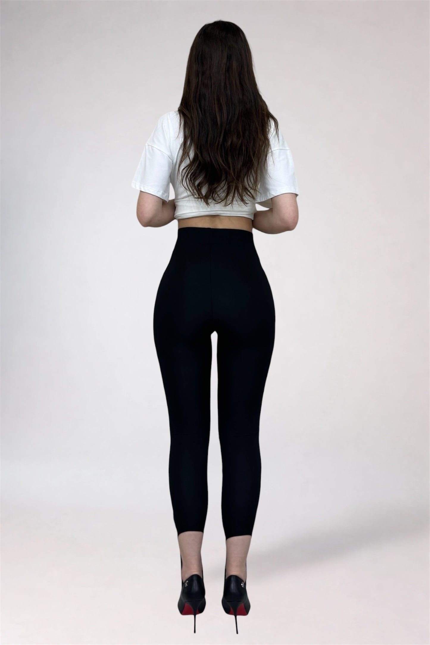 Person wearing black leggings and a white crop top on a plain background