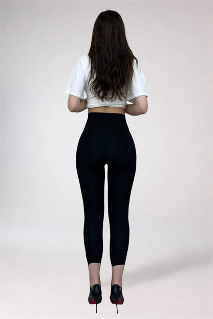 Person wearing black leggings and a white crop top on a plain background
