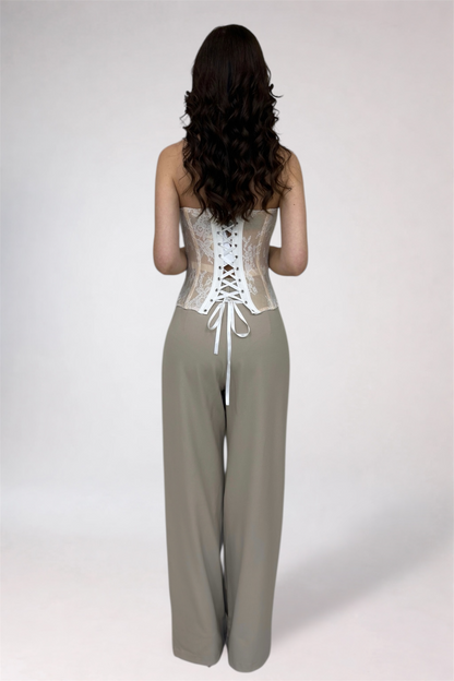 Woman wearing a white lace corset and beige pants on a white background