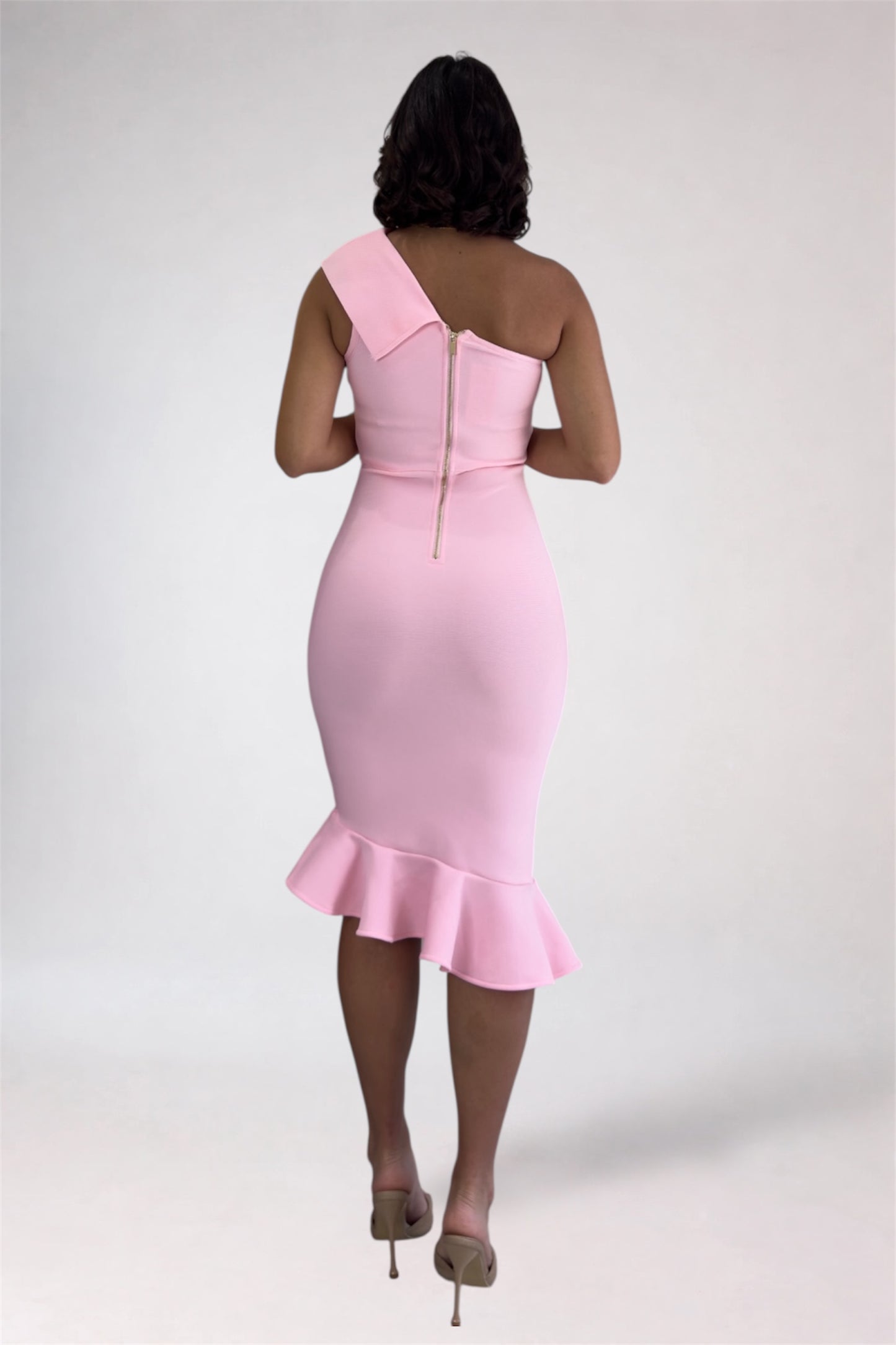 Woman wearing a pink one-shoulder dress with a ruffled hem on a white background