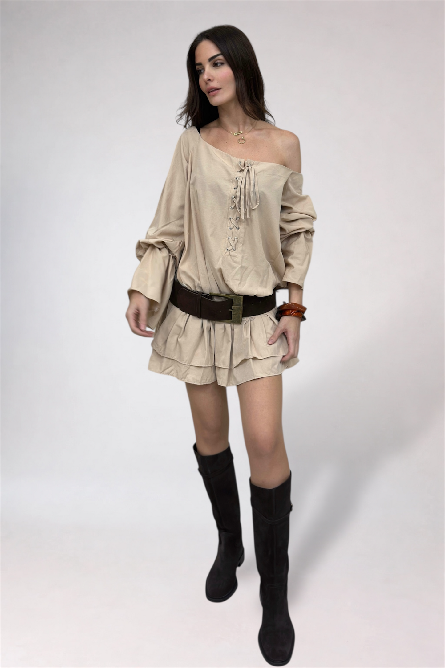 Woman wearing a beige off-shoulder top and skirt with black knee-high boots on a white background