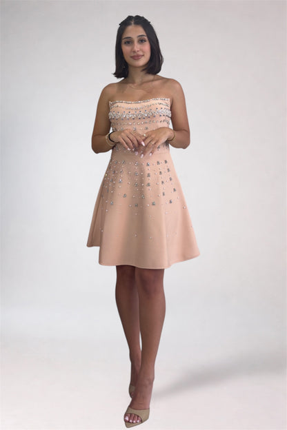 Woman wearing a strapless beige dress with floral embellishments on a white background