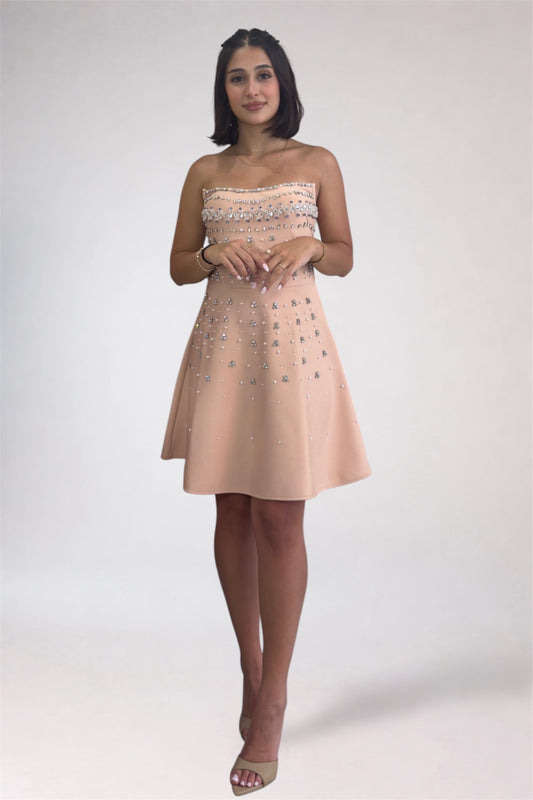 Woman wearing a strapless beige dress with floral embellishments on a white background