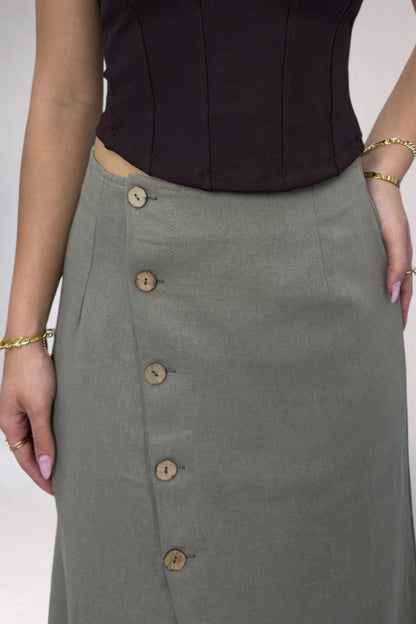 Person wearing a black top and green skirt with button details on a white background