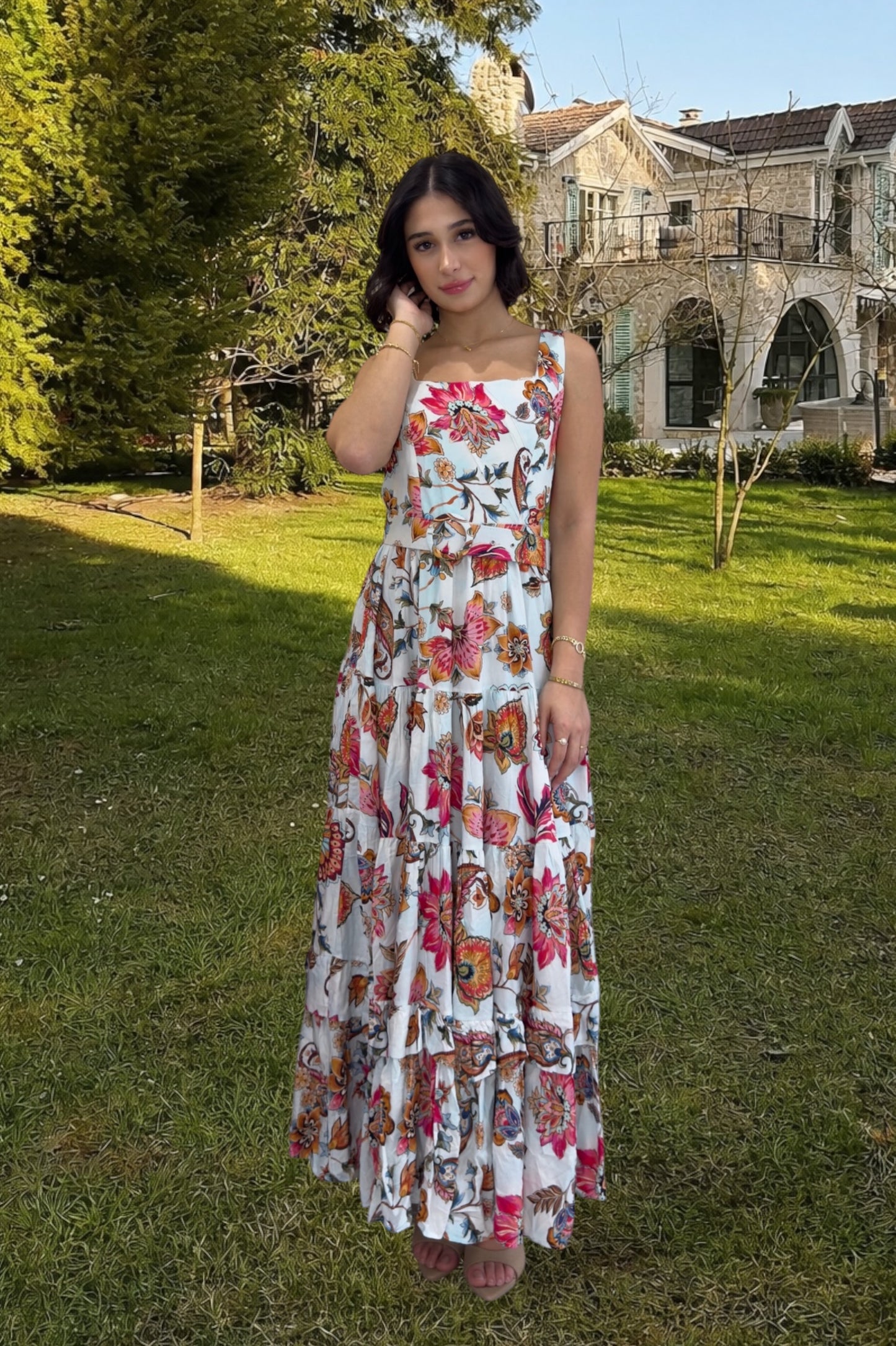 Woman in a floral dress standing in a garden with a building in the background