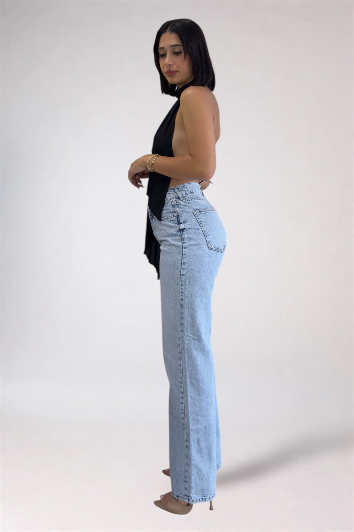 Woman wearing light blue jeans and a black top on a white background