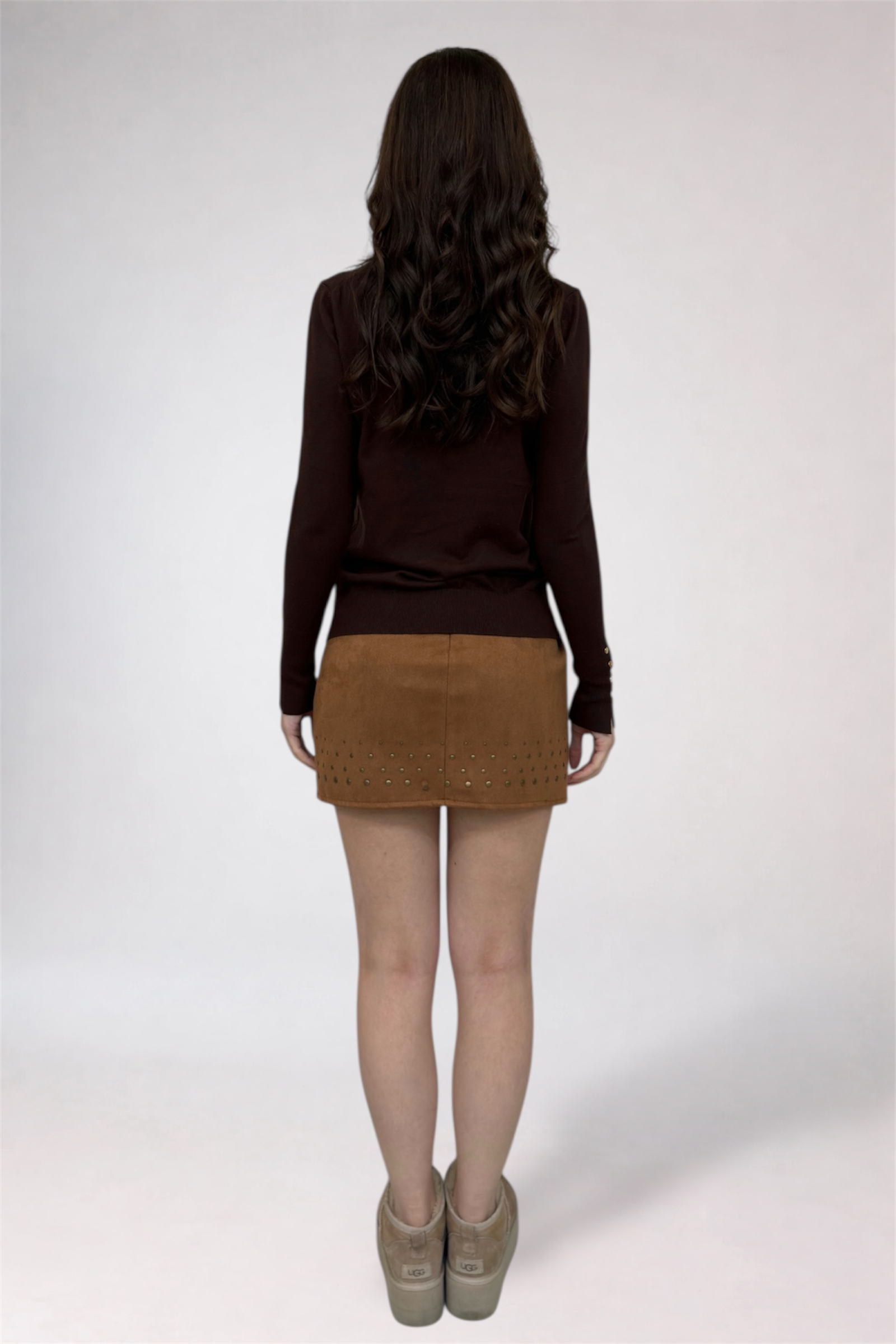Person wearing a brown sweater and tan skirt on a white background