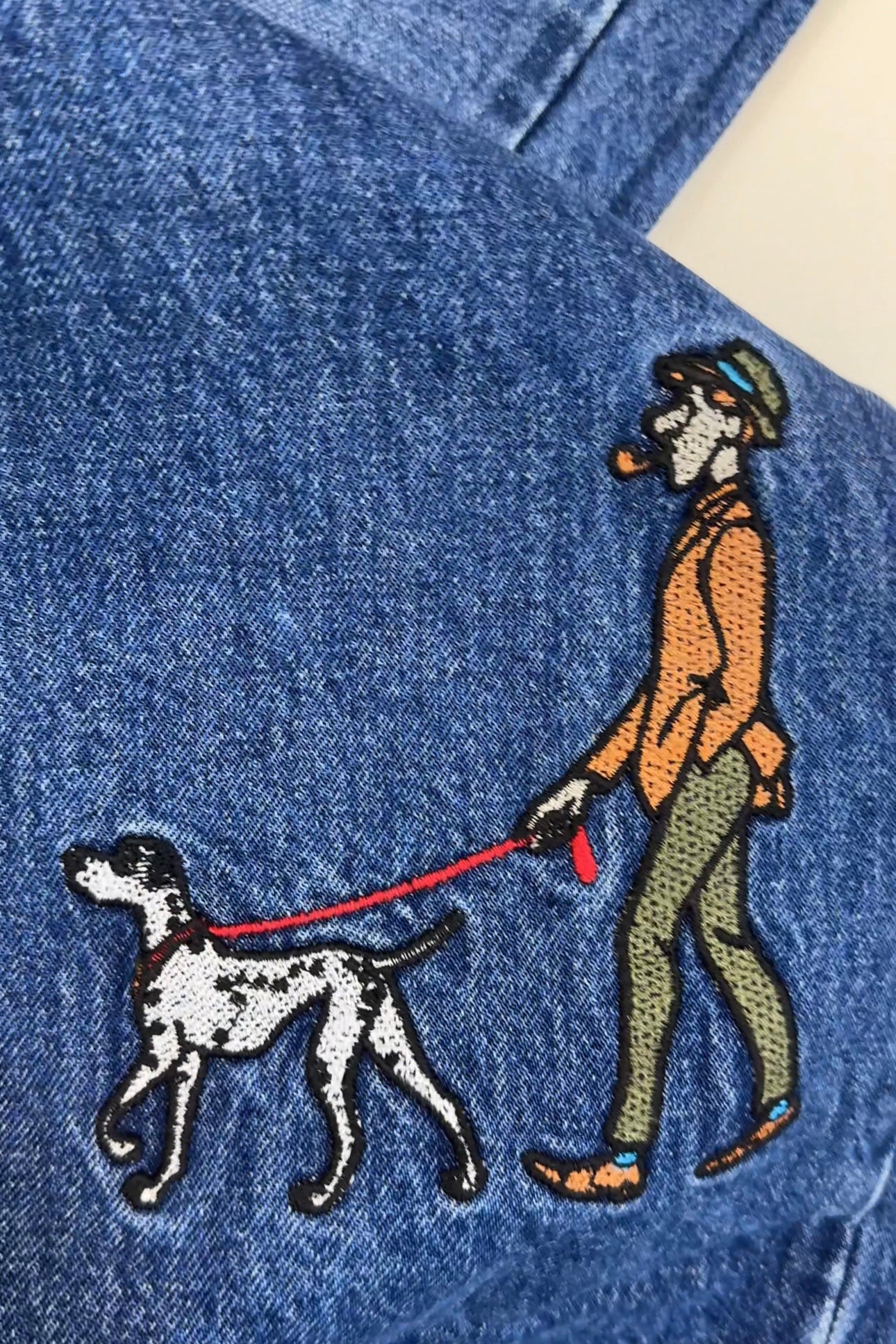 Embroidered design on denim fabric of a person walking a dog.