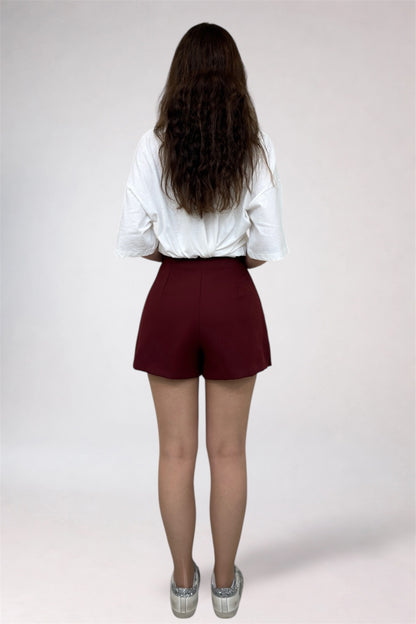 Person wearing a white blouse and maroon shorts on a plain background