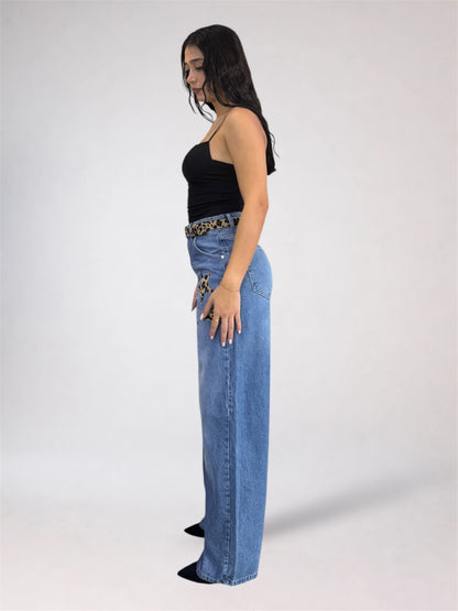 A woman stands in profile wearing a black strapless top, a leopard-print belt, and high-waisted wide-leg blue jeans against a plain light gray studio background.