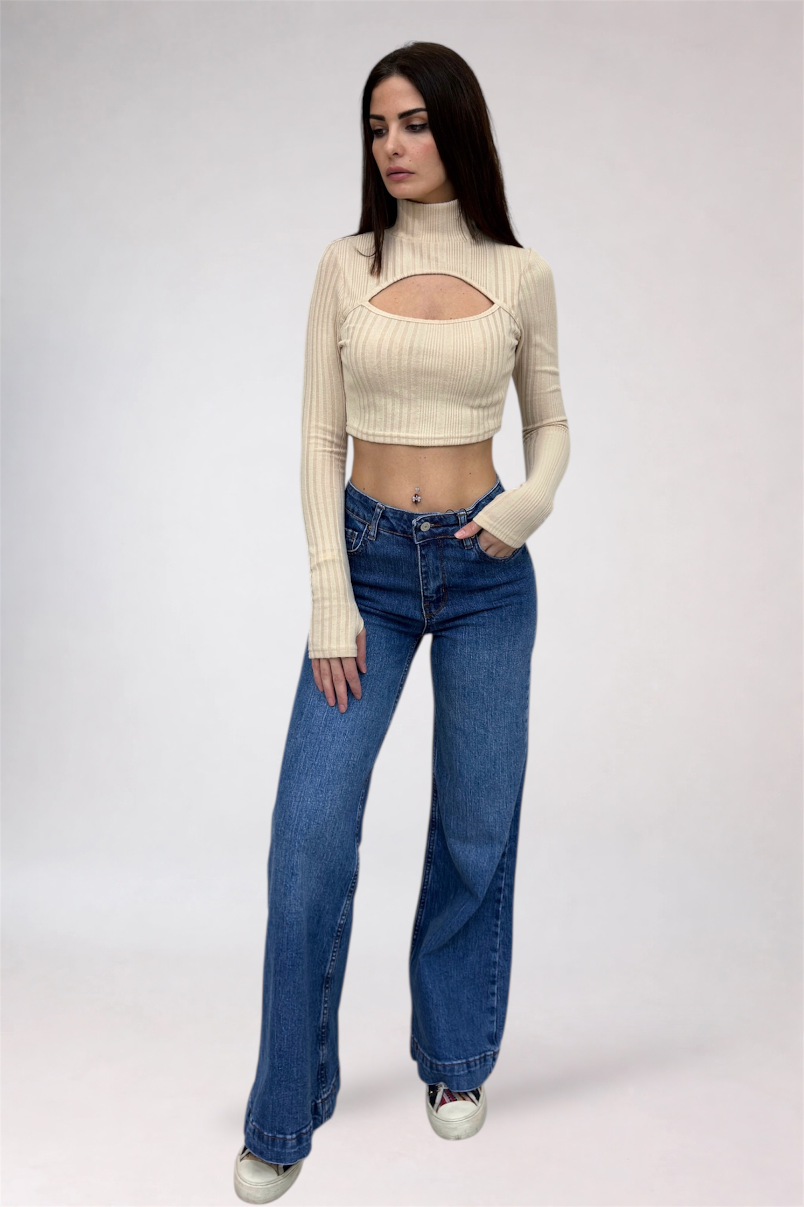 Woman wearing a beige long-sleeve crop top and blue jeans on a white background