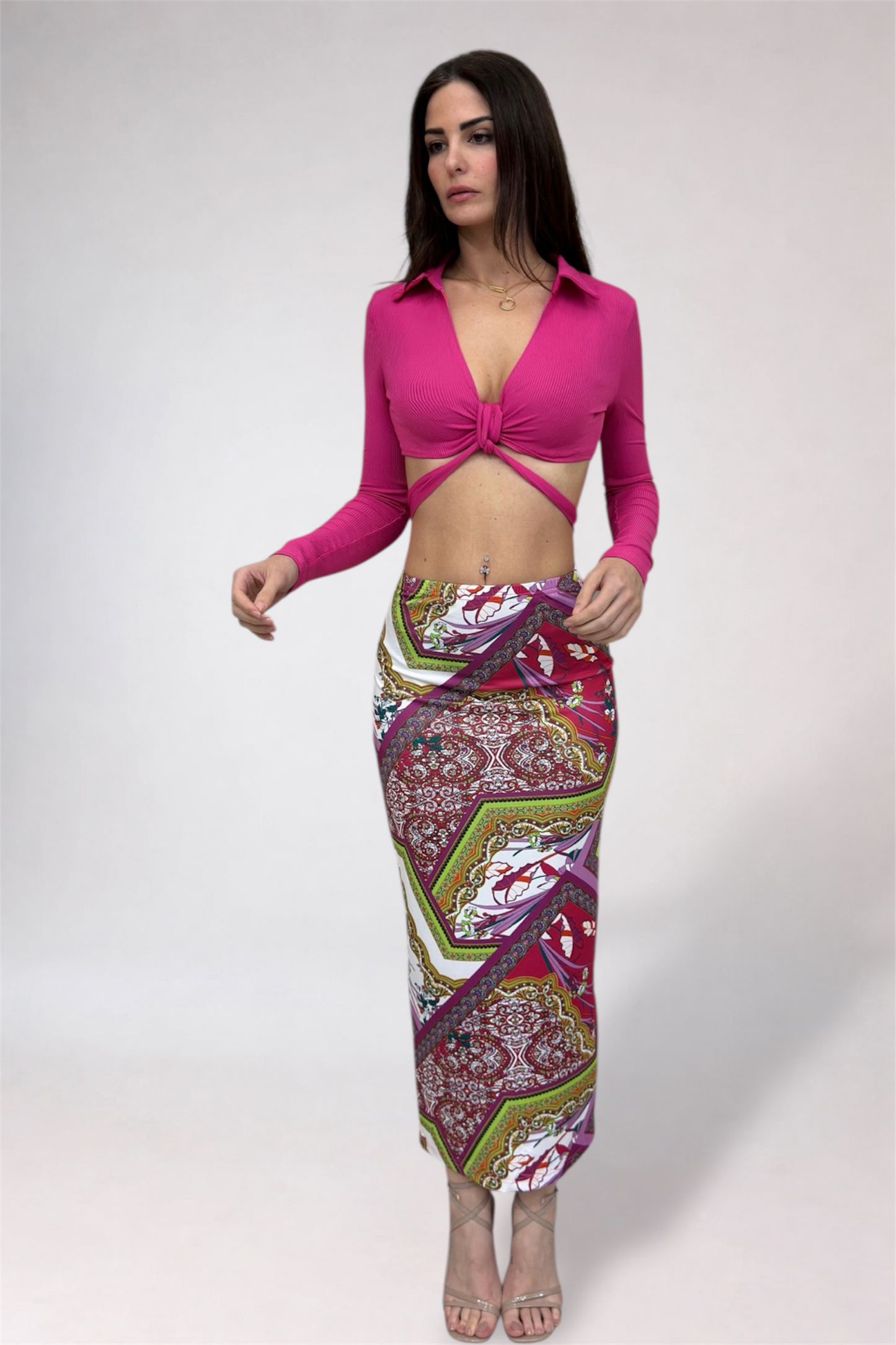 Woman wearing a bright pink top and patterned skirt on a white background