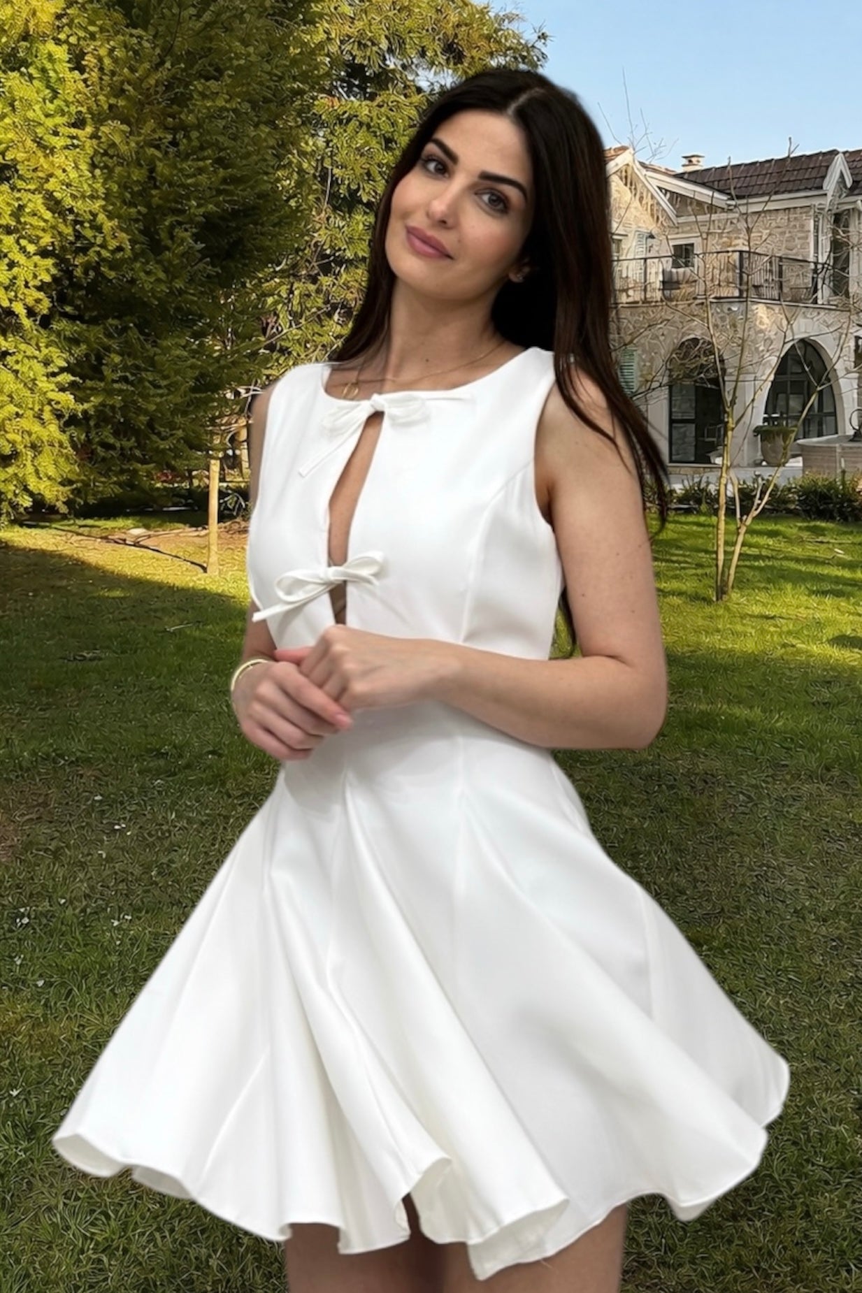 Woman in a white dress standing outdoors with greenery and a building in the background