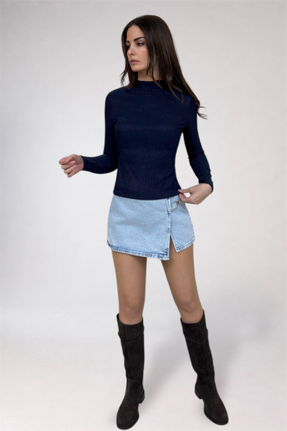 Woman wearing a navy long-sleeve top, light blue denim skirt, and black knee-high boots on a white background