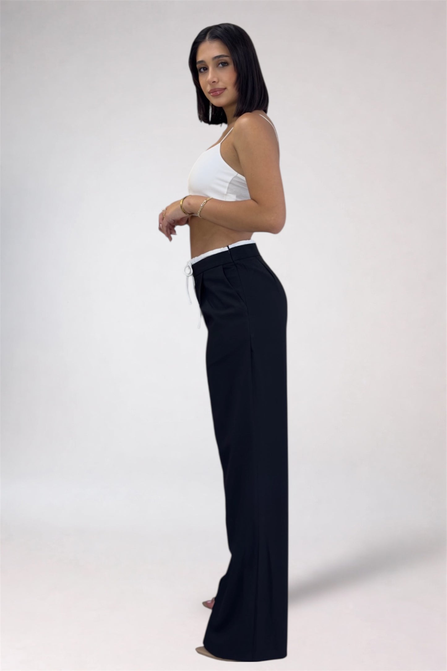 Woman wearing a white top and black pants on a plain background