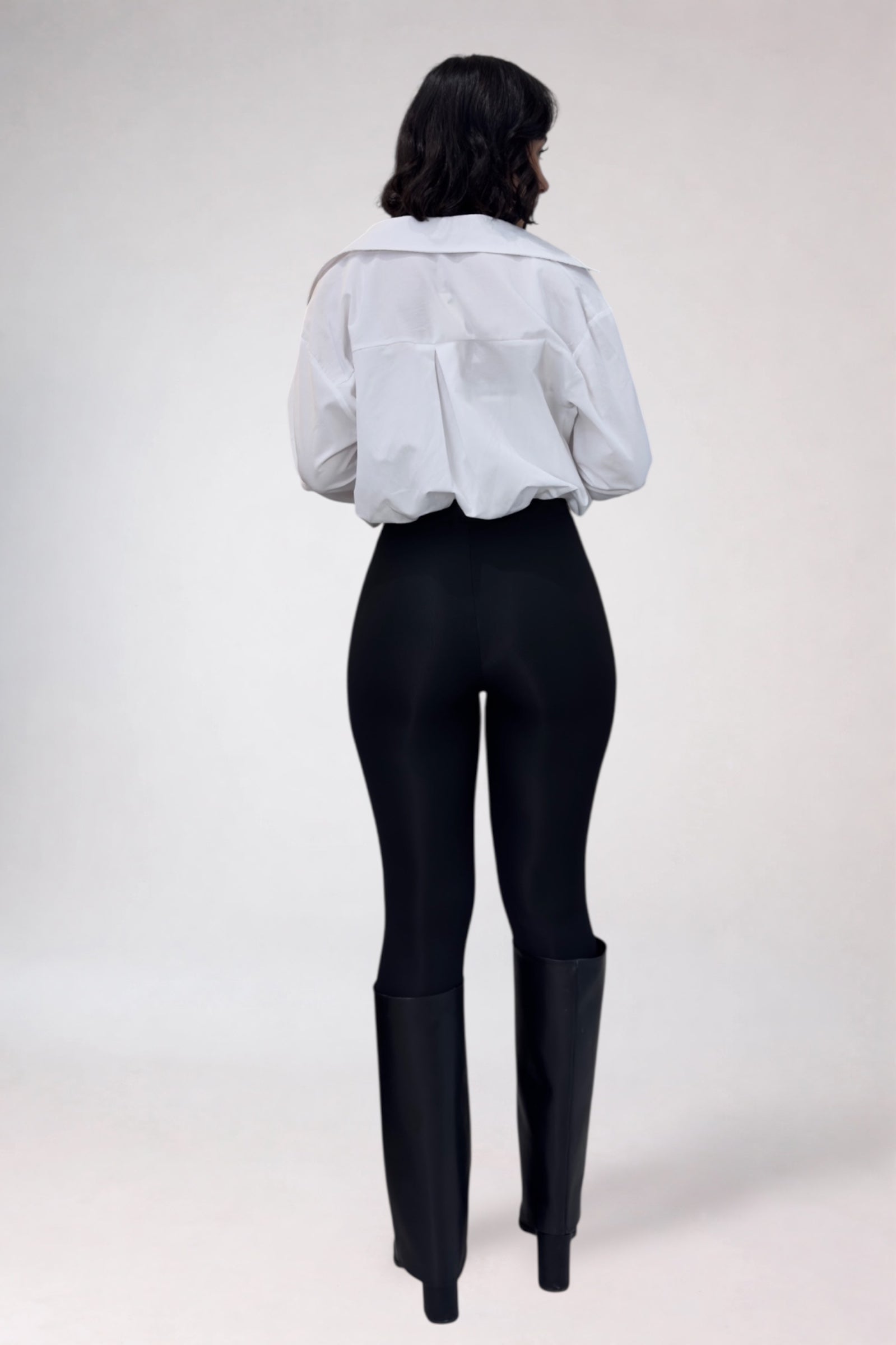Person wearing a light gray shirt, black pants, and black boots on a white background