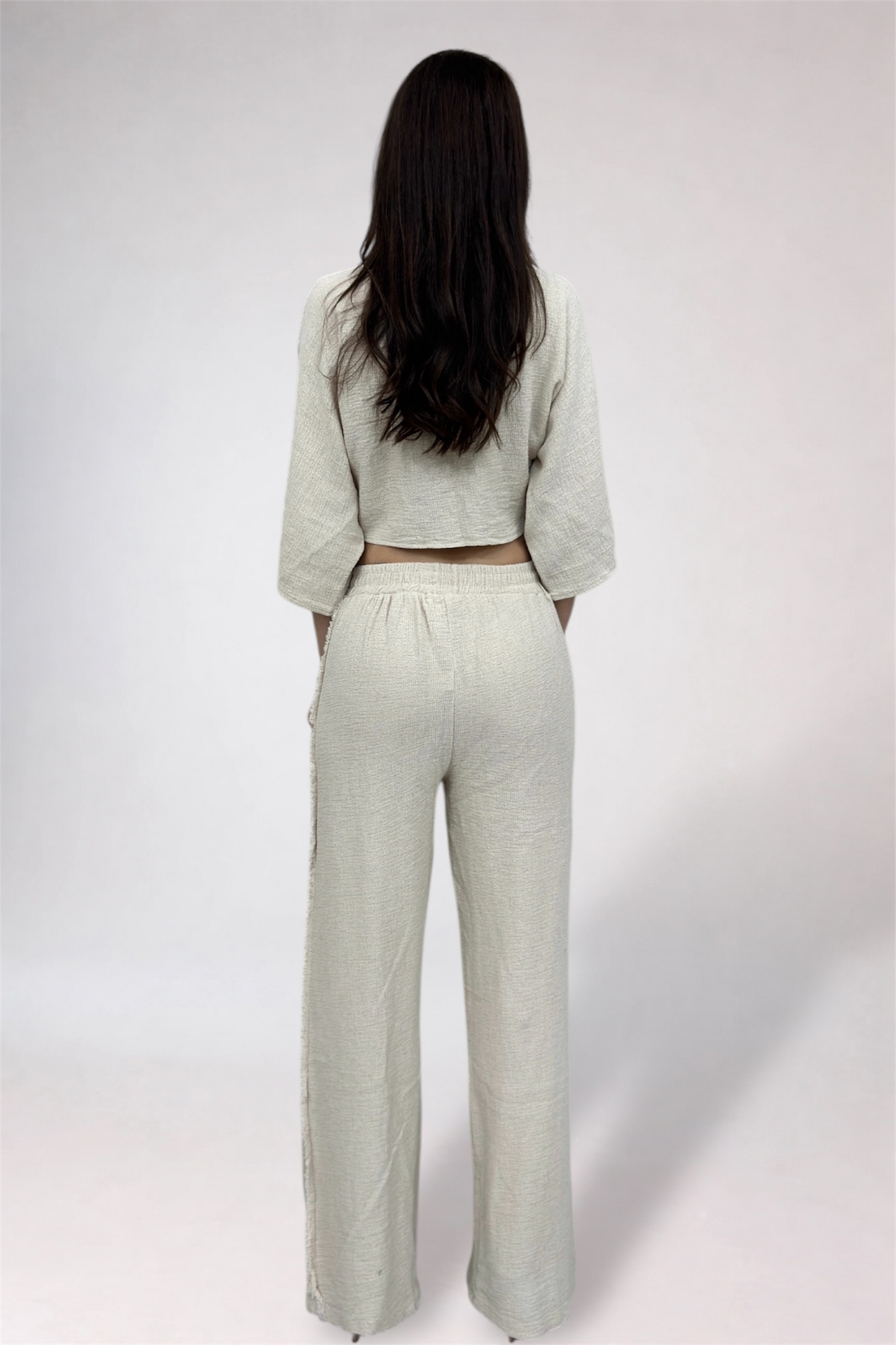 Person wearing a light-colored outfit with wide-leg pants on a white background