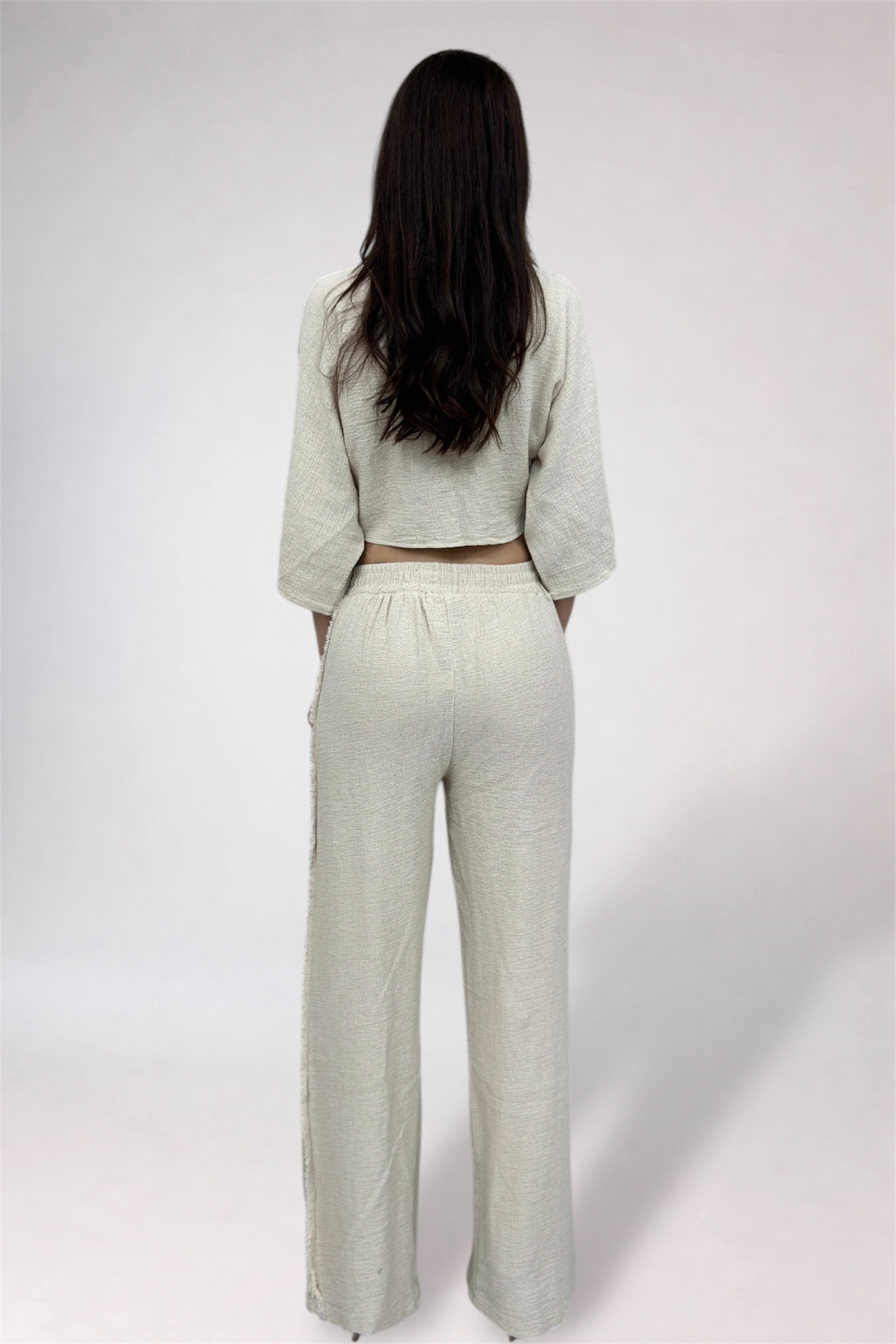 Person wearing a light-colored outfit with wide-leg pants on a white background